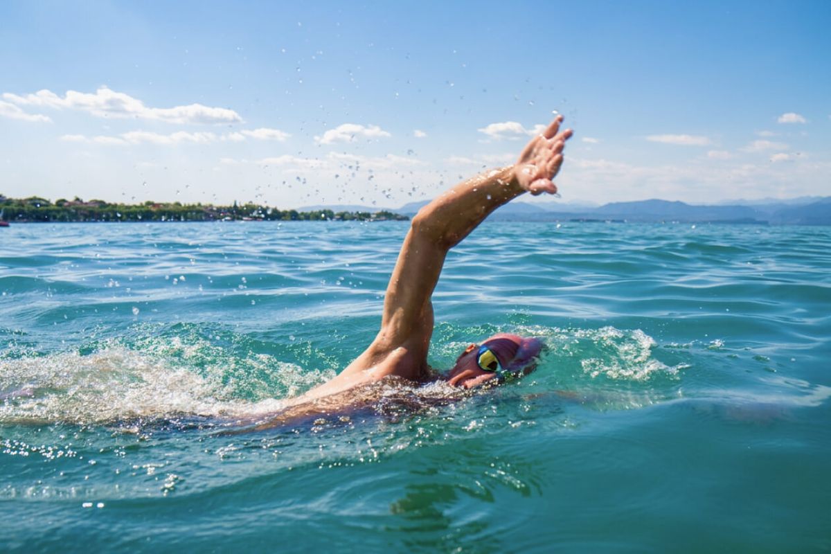 Nuotatore in acque libere durante il recupero della bracciata a stile libero, con la costa del lago sullo sfondo