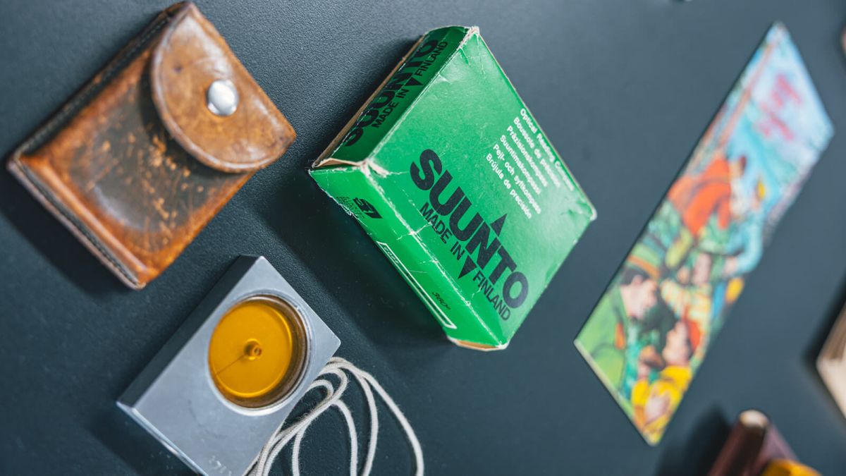 Pezzi d'archivio Suunto esposti alla mostra: una custodia in pelle consumata, una bussola in metallo e la scatola verde Suunto Made in Finland
