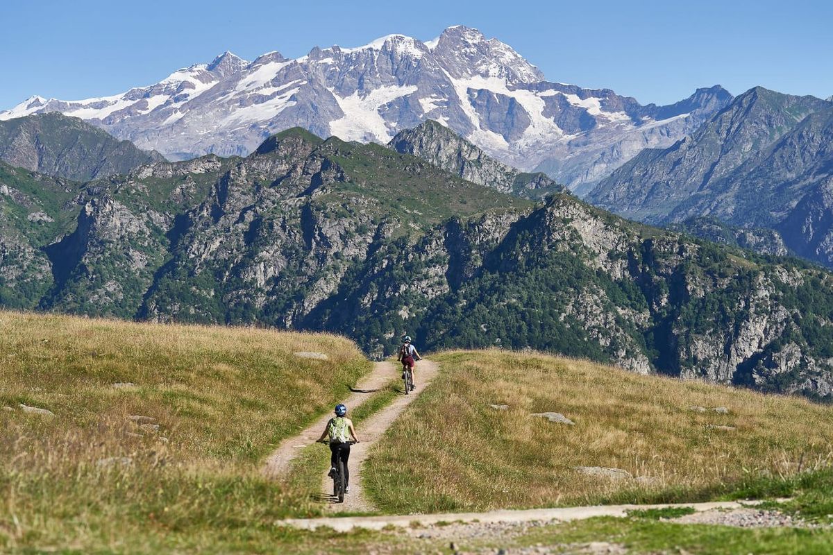 Due ciclisti su uno sterrato in quota con il massiccio innevato del Monte Rosa sullo sfondo