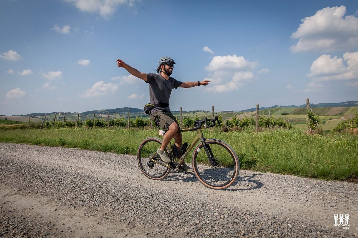 Ciclista gravel a braccia aperte su una strada bianca tra le colline piemontesi